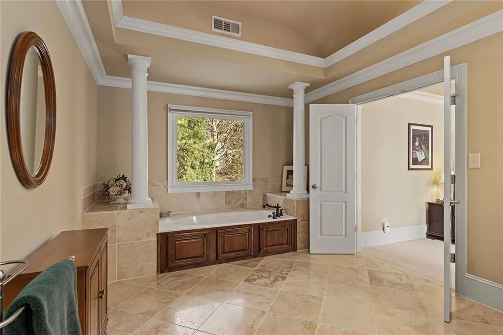 Bathroom featuring decorative columns, crown molding, and a tub