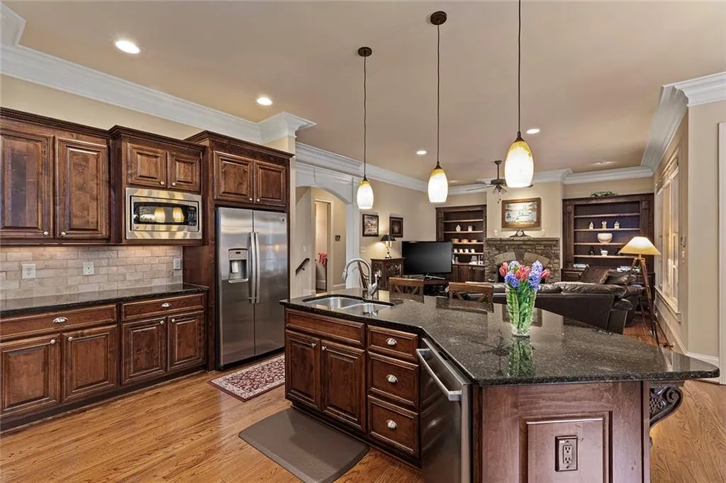 Kitchen with appliances with stainless steel finishes, decorative light fixtures, sink, dark stone counters, and a center island with sink