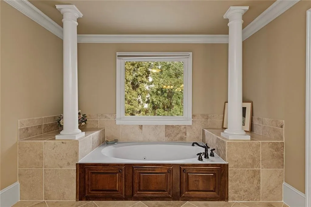 Bathroom with ornate columns, crown molding, tile patterned flooring, and a bath