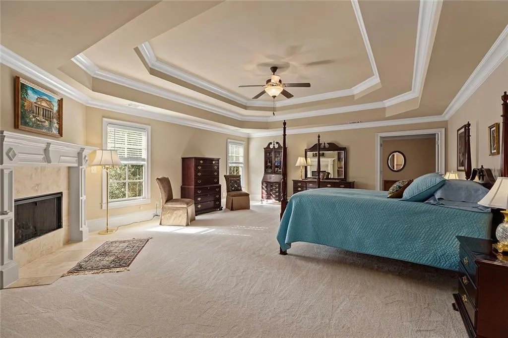 Bedroom with light carpet, ornamental molding, a tile fireplace, and a raised ceiling