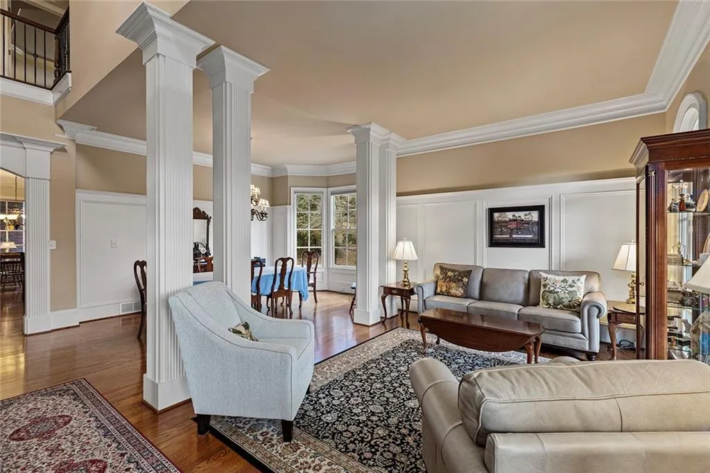 Living room featuring decorative columns, ornamental molding, dark hardwood / wood-style floors, and a notable chandelier