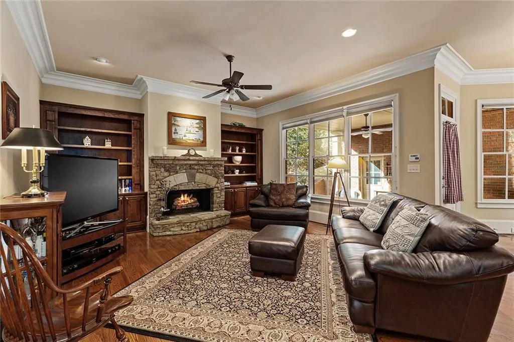 Living room with wood-type flooring, a stone fireplace, ceiling fan, and crown molding