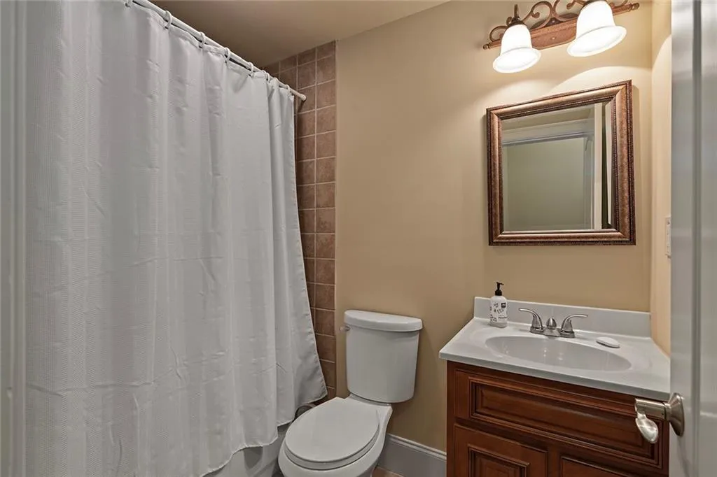 Full bathroom in basement featuring vanity, toilet, and shower / bathtub combination with curtain
