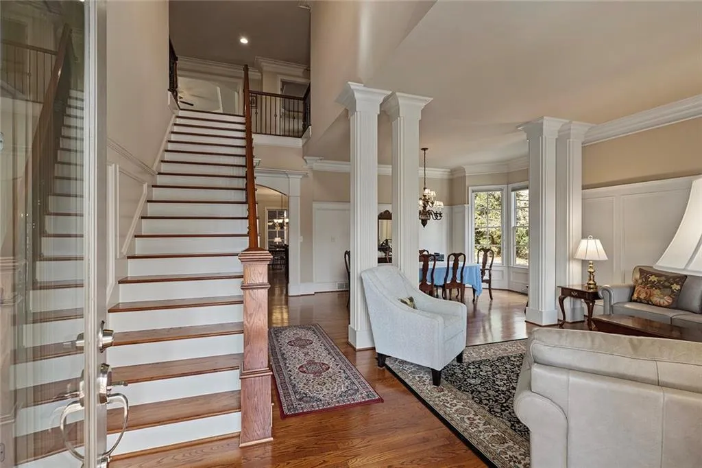 Living room featuring decorative columns, crown molding, a notable chandelier, and dark hardwood / wood-style flooring