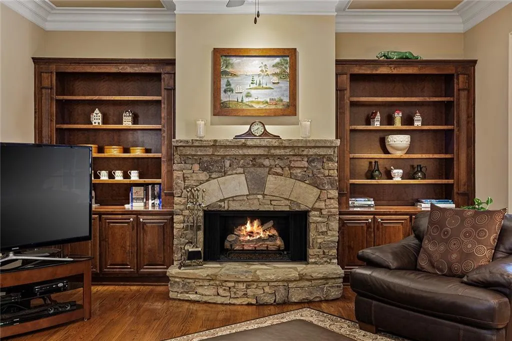 Living room with ornamental molding, a stone fireplace, and dark wood-type flooring