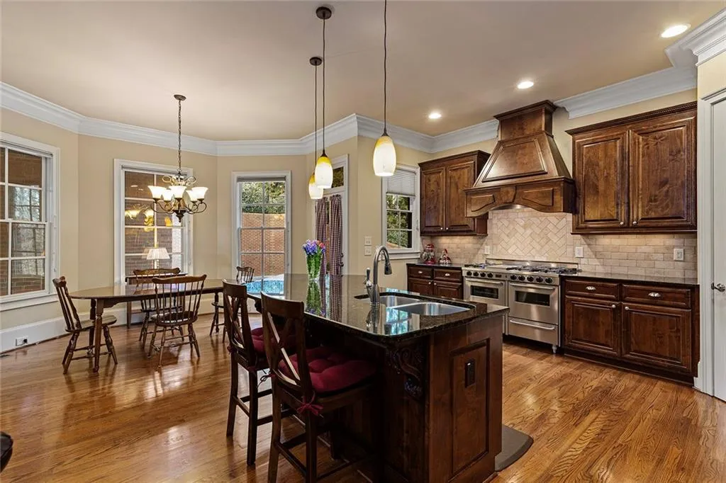 Kitchen with dark stone countertops, a kitchen breakfast bar, range with two ovens, custom range hood, and a center island with sink