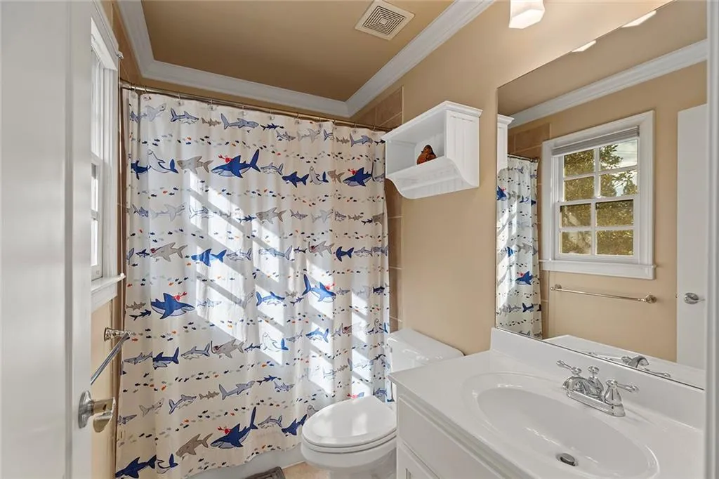 En suite bathroom with a shower with curtain, ornamental molding, vanity, and toilet