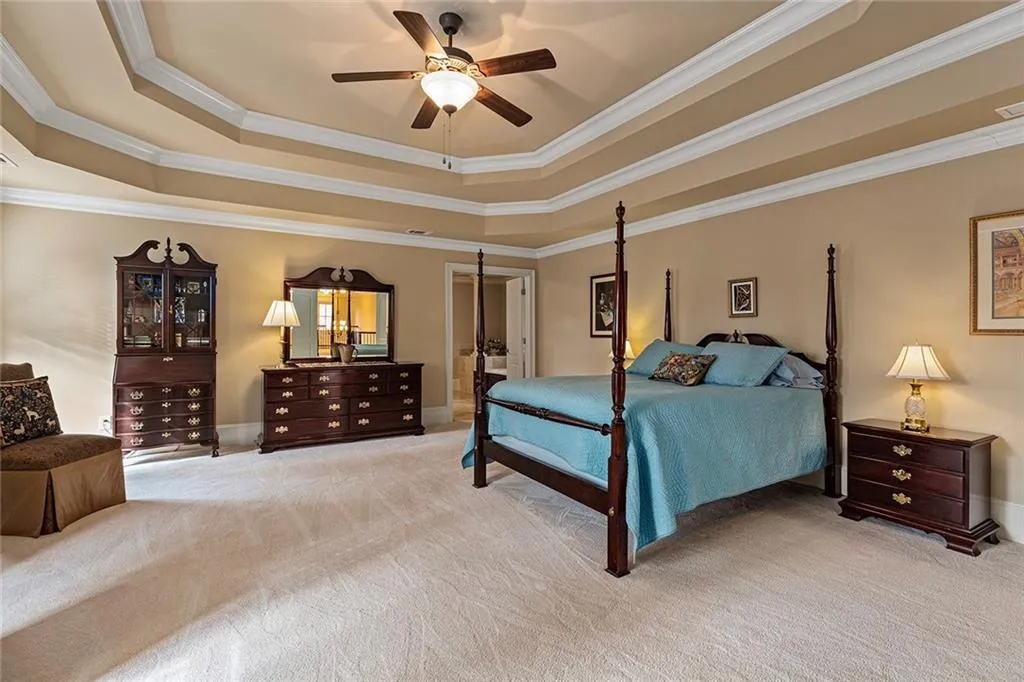 Carpeted bedroom with ceiling fan, ornamental molding, and a tray ceiling