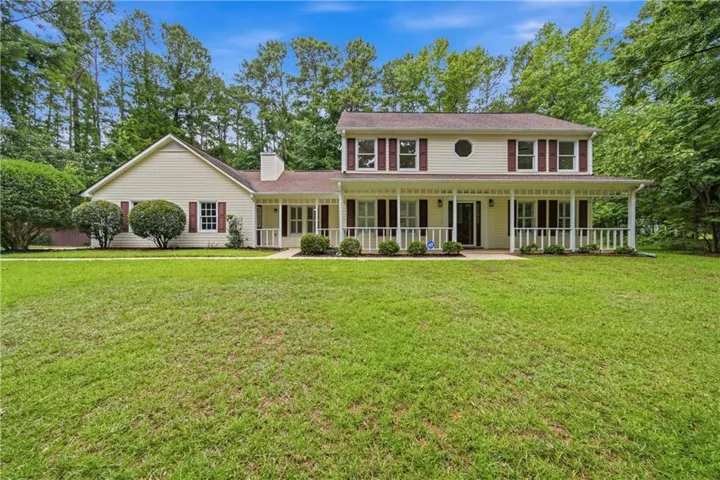 Two-story residence featuring light-colored siding, a full-width front porch with white railings, and dark red shutters