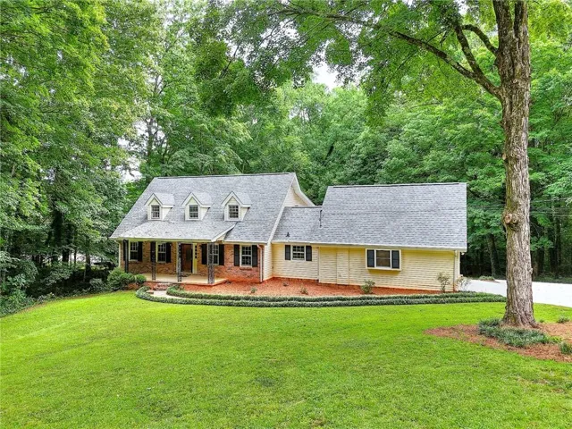 Front exterior featuring dormer windows, a covered porch with dark columns, brick accents, and light-toned siding