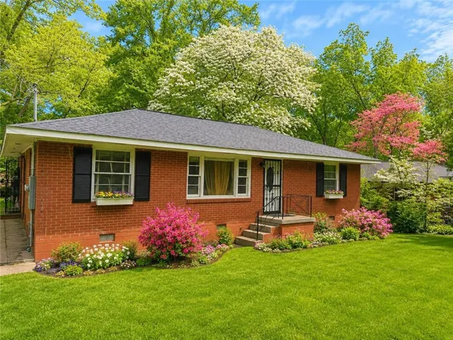 Brick ranch-style residence featuring a dark shingle roof and black louvered shutters