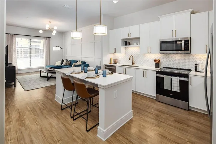 Kitchen featuring stainless steel appliances, a kitchen island with sink, a kitchen bar, and white cabinets