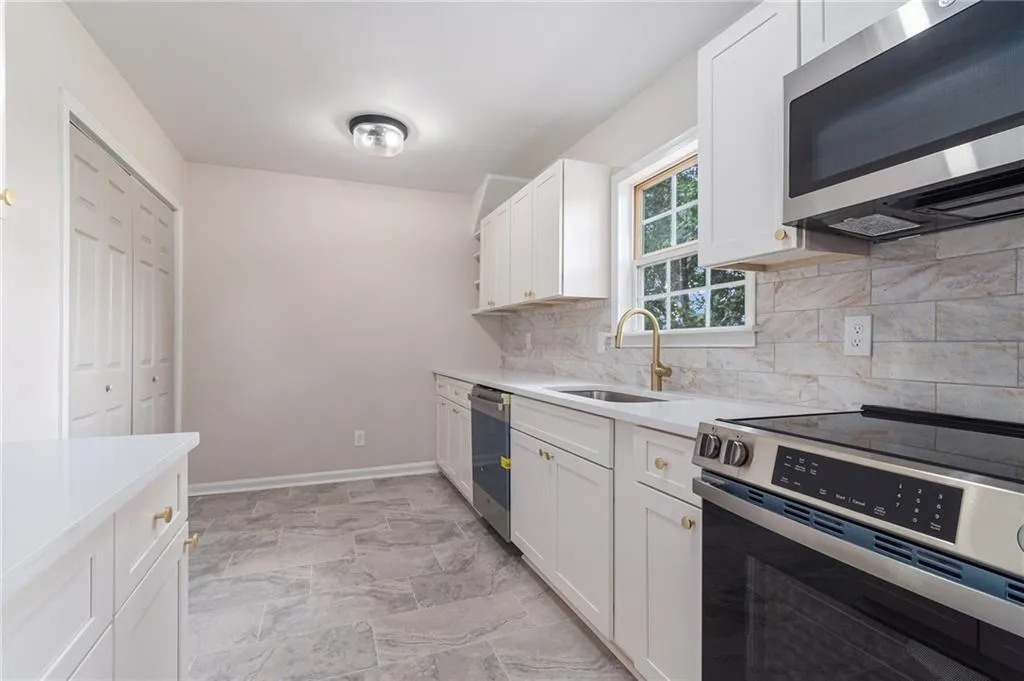 Kitchen with stainless steel appliances, white cabinets, backsplash, and light stone counters