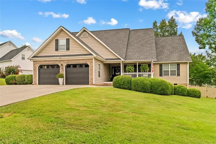 Siding exterior with a covered porch, attached two-car garage, and established landscaping
