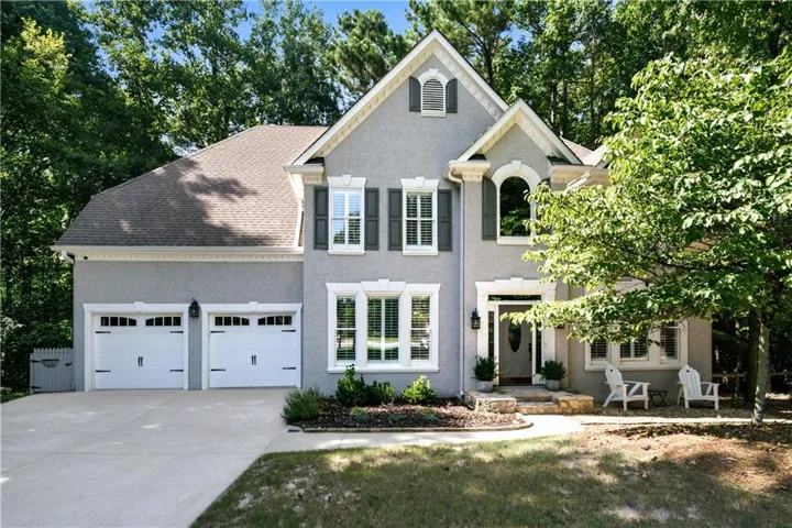Stucco exterior featuring a two-car garage with carriage-style doors, prominent arched window, white trim accents, and dark shutters