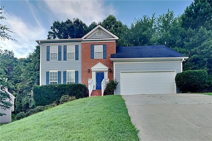 Traditional two-story residence featuring a brick and siding exterior, a prominent blue entry door, and an attached two-car garage