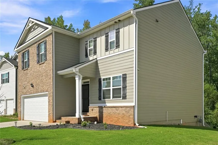 Two-story colonial featuring brick and siding exterior with gabled roofline, front-load garage, and manicured lawn with mature landscaping