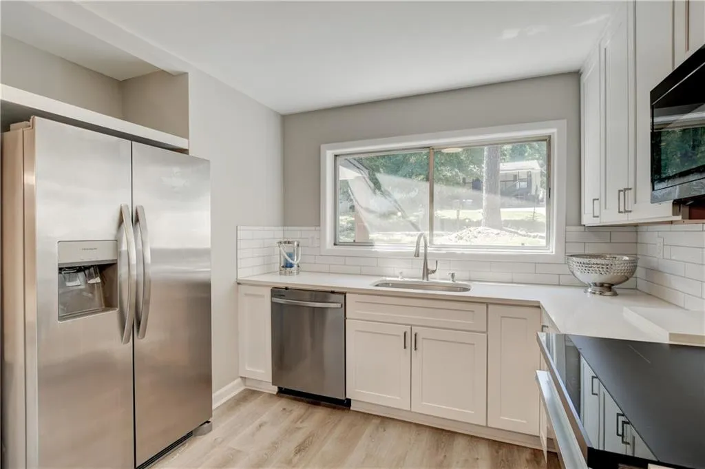 Kitchen featuring appliances with stainless steel finishes, white cabinets, light stone countertops, light wood finished floors, and decorative backsplash