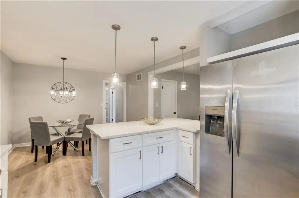 Kitchen featuring stainless steel fridge, hanging light fixtures, light wood-style flooring, and white cabinetry
