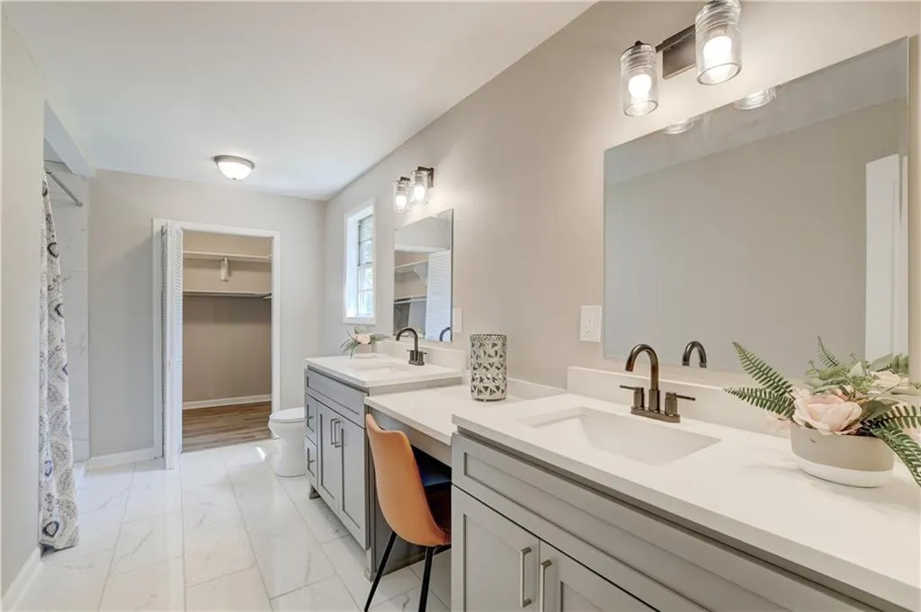 Full bathroom with two vanities, light marble finish floors, a walk in closet, and a shower with shower curtain