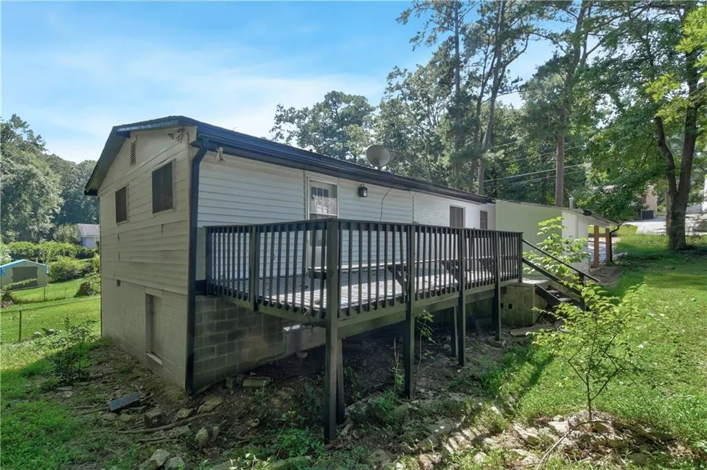 Back of house with a deck, a lawn, and view of scattered trees
