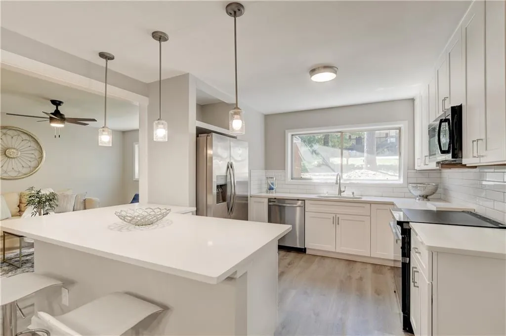 Kitchen with black appliances, a breakfast bar area, pendant lighting, backsplash, and light wood finished floors