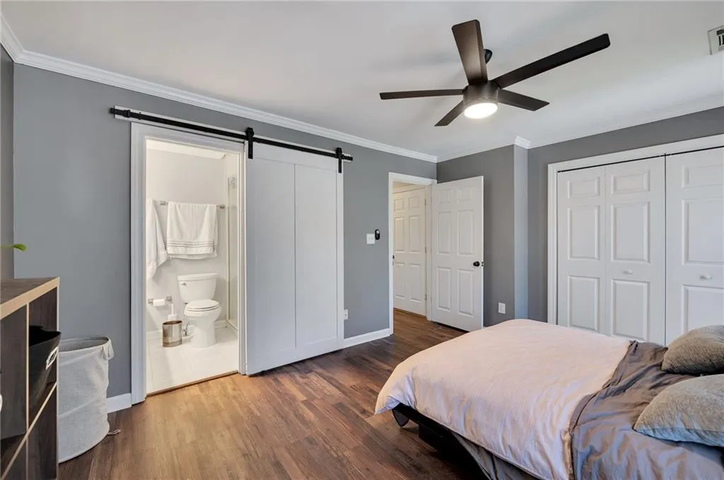 Tiled bedroom with a barn door, ensuite bath, ceiling fan, and crown molding