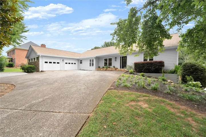 Ranch-style residence featuring light-toned horizontal siding, a two-car garage with panel doors, a paved driveway, and mature landscaping