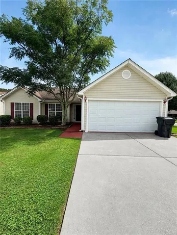 Single-story residence featuring light-colored siding, an attached garage, a mature front tree, and a concrete driveway
