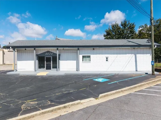 White exterior with a gray-shingled roof, featuring a covered entry and a paved parking area with marked spaces