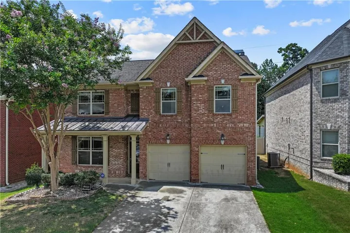 Brick exterior with a gabled roofline, covered front entry, two-car garage, and mature landscaping