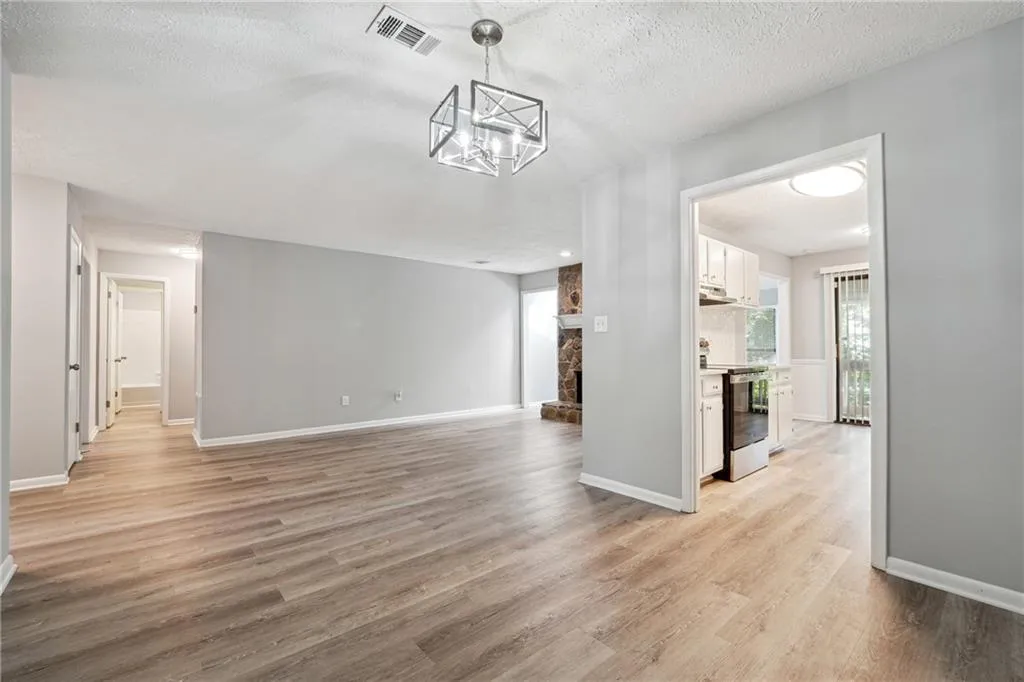 Unfurnished living room with a chandelier, a stone fireplace, a textured ceiling, and light hardwood / wood-style flooring