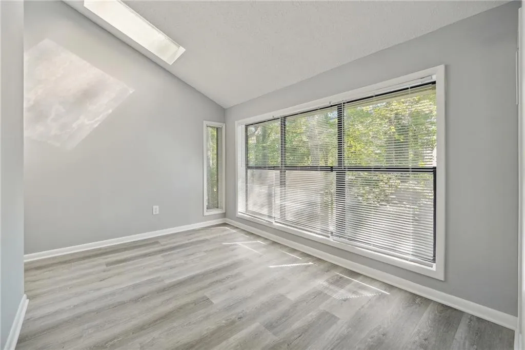 Empty room with lofted ceiling with skylight, a textured ceiling, and light hardwood / wood-style flooring