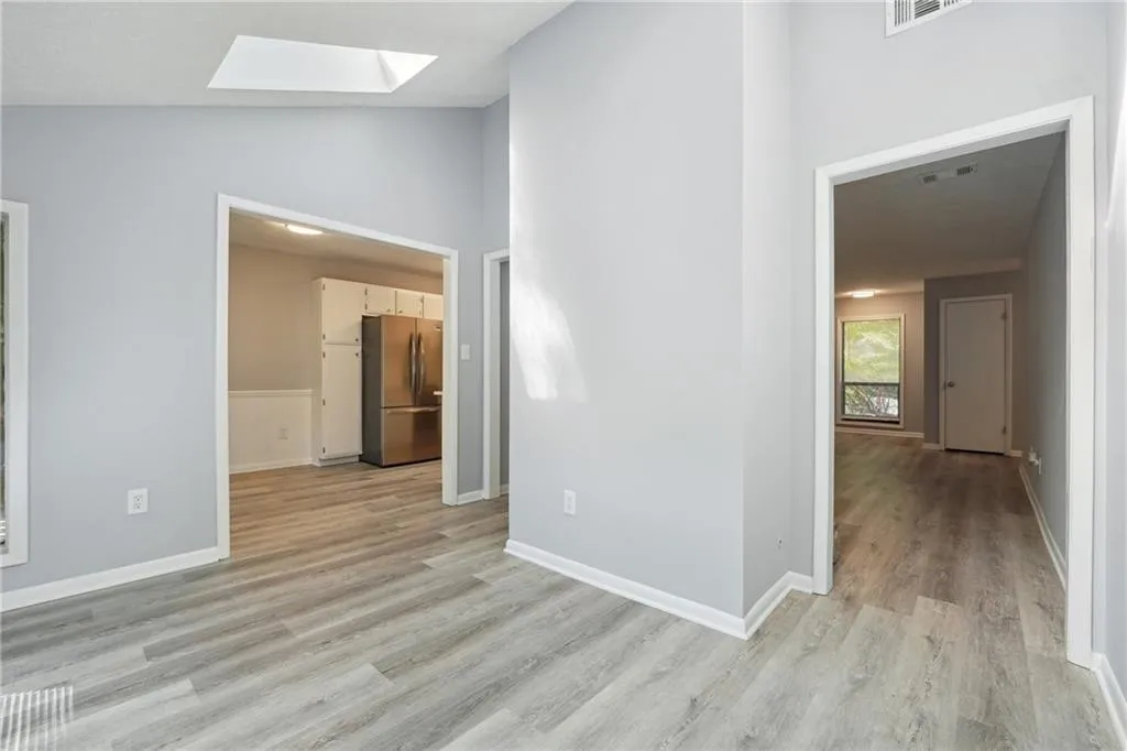 Empty room with vaulted ceiling with skylight and light hardwood / wood-style floors