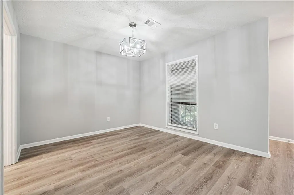 Spare room with a notable chandelier, a textured ceiling, and light wood-type flooring