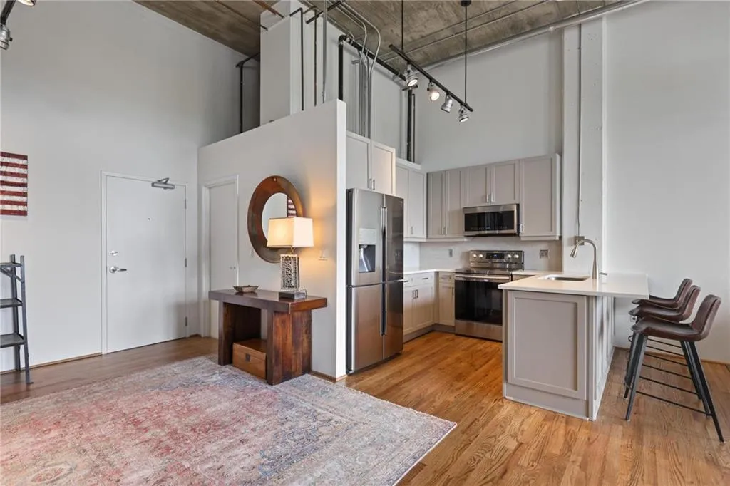 Industrial-style kitchen featuring exposed concrete ceilings, wood-finish flooring, stainless steel appliances, cabinetry with light-toned finish, and a stone-topped peninsula