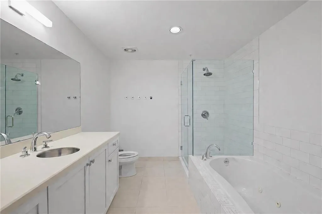 Bathroom featuring a white vanity with a neutral countertop, an undermount sink, a jetted soaking tub, and a glass-enclosed shower with subway tile surround