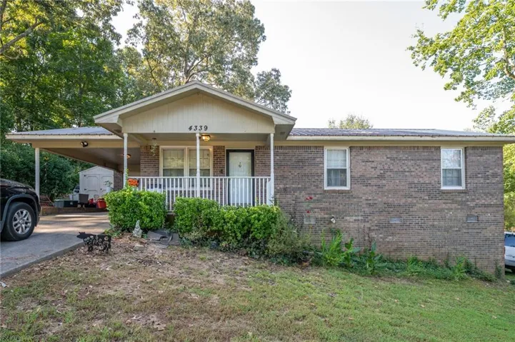 Brick exterior featuring a covered front porch, white railings, and an attached carport