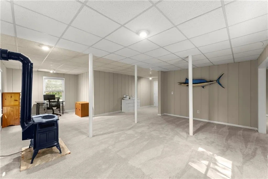 Basement with a drop ceiling, carpet, and a wood stove