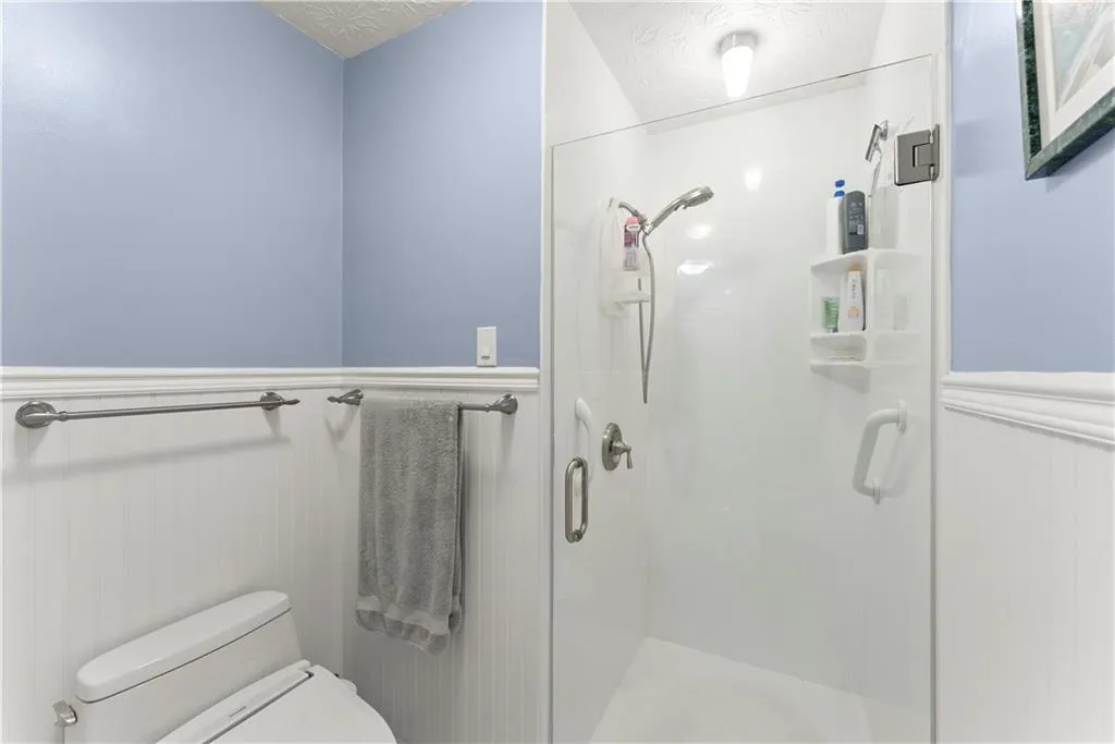 Bathroom with wainscoting, a shower stall, and a textured ceiling