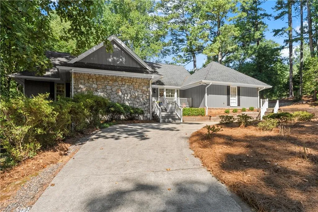 View of front of home with a porch, driveway, stone siding, and roof with shingles