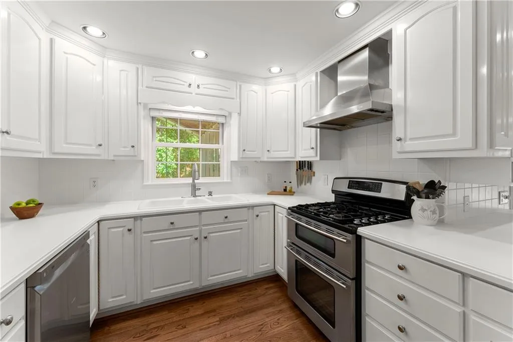Kitchen featuring appliances with stainless steel finishes, wall chimney range hood, dark wood-style flooring, white cabinetry, and recessed lighting