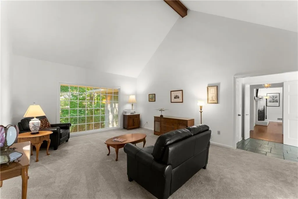 Carpeted living area with high vaulted ceiling and beam ceiling