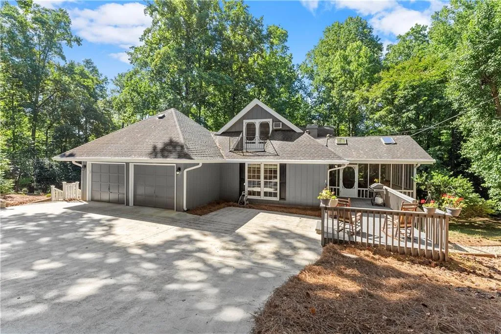 Back of house with roof with shingles, an attached garage, driveway, a sunroom, and view of wooded area