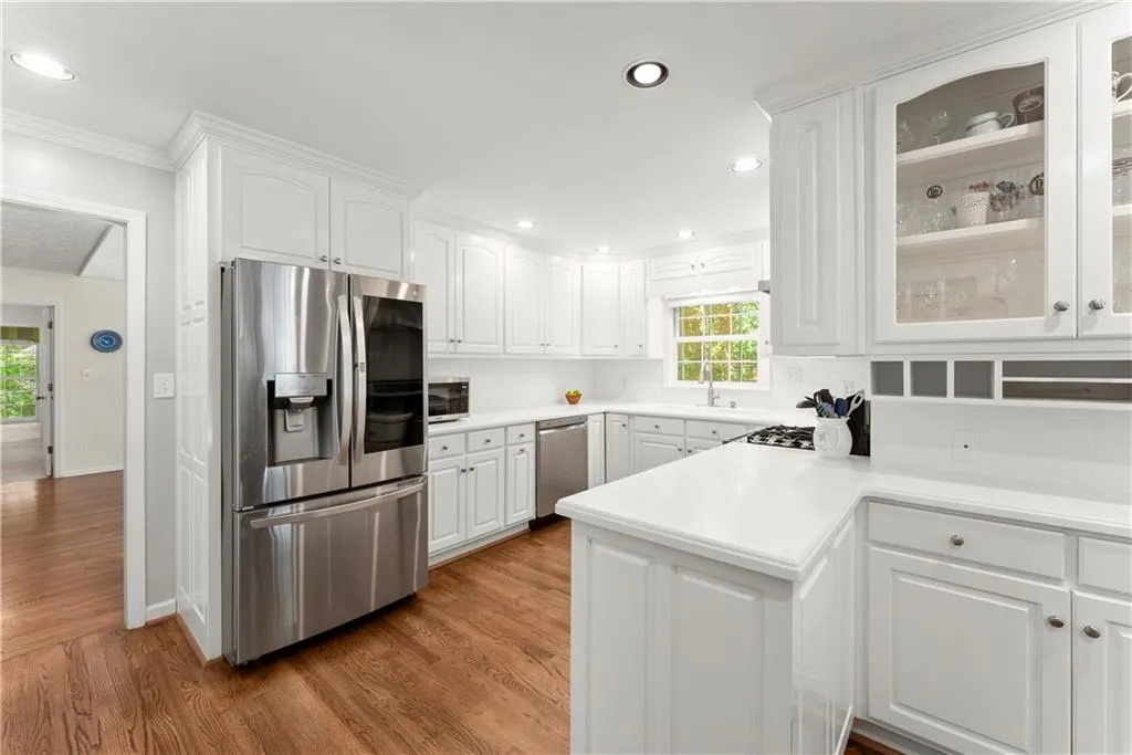 Kitchen with stainless steel appliances, white cabinetry, glass insert cabinets, crown molding, and wood finished floors