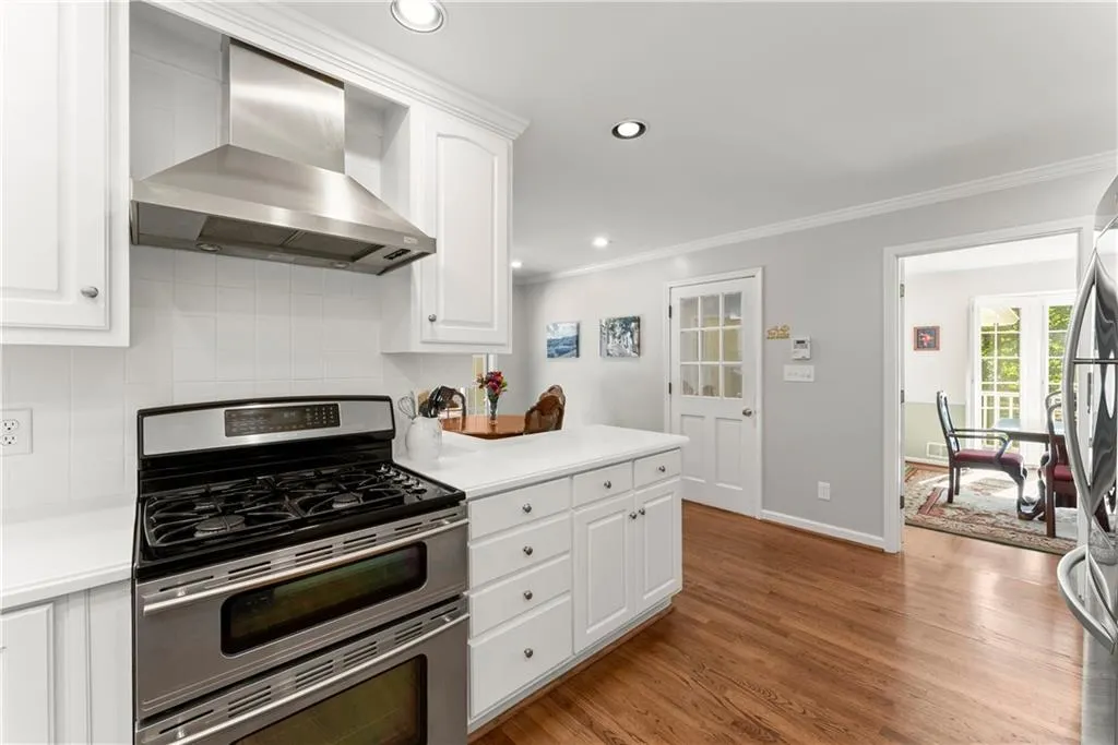 Kitchen featuring appliances with stainless steel finishes, wall chimney exhaust hood, crown molding, tasteful backsplash, and white cabinets