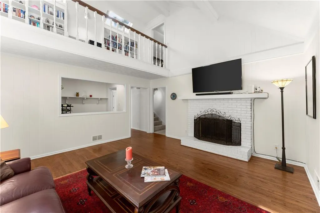 Living room featuring high vaulted ceiling, a brick fireplace, wood finished floors, stairs, and beam ceiling