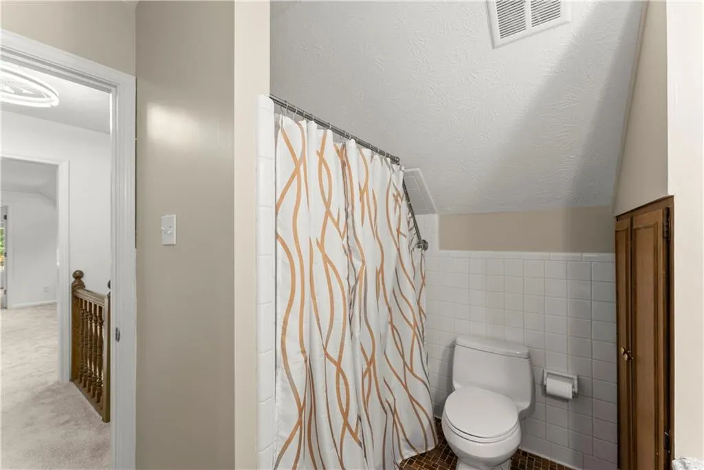 Full bath with vaulted ceiling, tile walls, a textured ceiling, and curtained shower