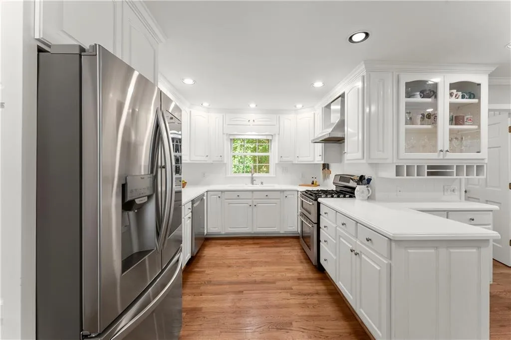 Kitchen with stainless steel appliances, light wood-style floors, recessed lighting, glass insert cabinets, and white cabinetry