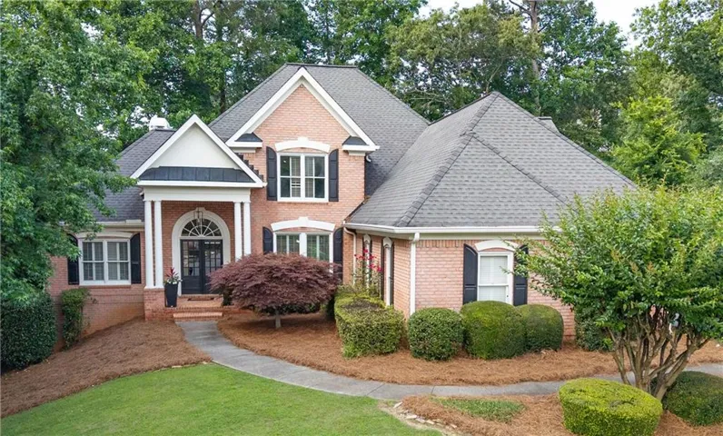 Brick-clad exterior with a prominent gabled entry portico, dark shingled roof, and black-shuttered windows